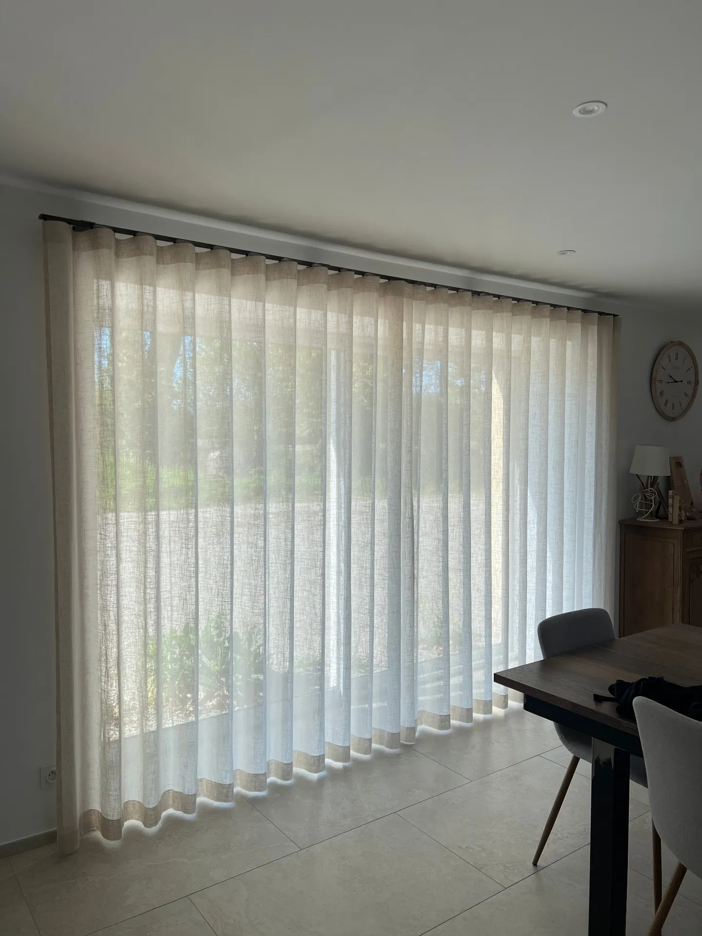 Voilages crème toute hauteur le long d'une baie vitrée dans une salle à manger lumineuse